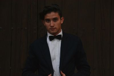 Portrait of handsome man wearing black suit while standing against wooden wall