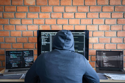 Rear view of man working against brick wall