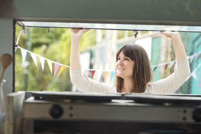 Smiling female owner working outside food truck seen through glass window