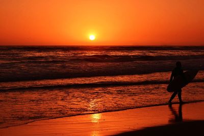 Silhouette man standing on beach against orange sky