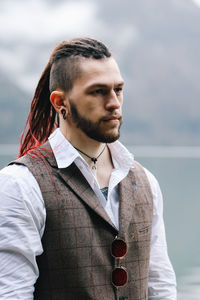 A brutal male hipster groom in a wedding suit in nature by the mountains and lake