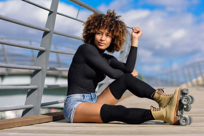 Thoughtful woman wearing roller skates while sitting on footbridge