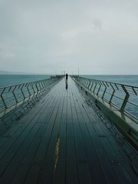 Rear view of man on footbridge over sea against sky