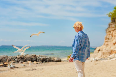 Elderly woman standing on the beach and looking into the distance