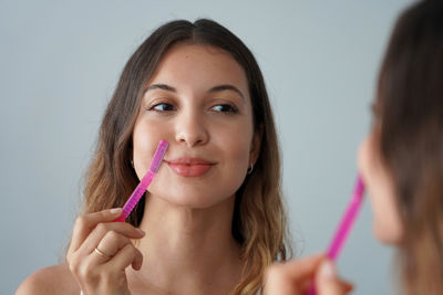 Portrait of young woman applying make-up against wall