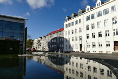 Canal by buildings in city against sky