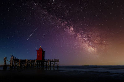 The milky way in the sky above an old wooden lighthouse on the sea
