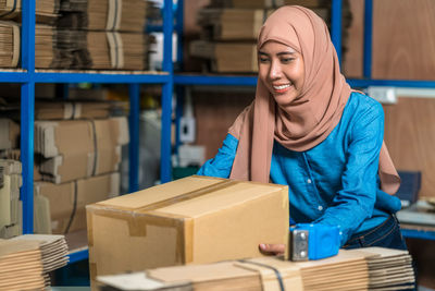 Warehouse muslim worker woman packing cardboard box with sticky tape in local warehouse 