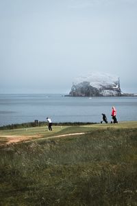 People on field by sea against sky