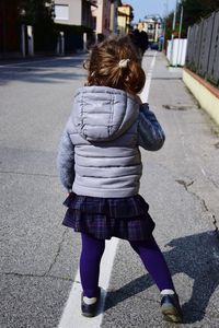 Rear view of girl standing on street during sunny day