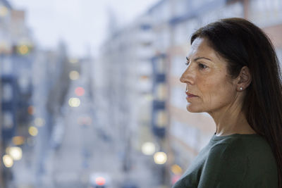 Profile view of mature woman standing next to window
