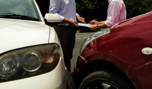 Midsection of men doing paperwork while standing by cars