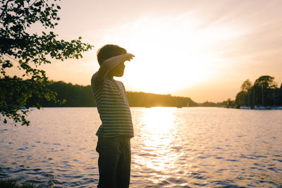 Man standing by lake against sky during sunset