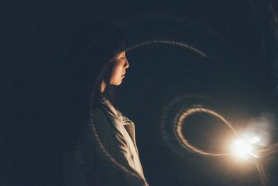 Woman standing by illuminated light bulb in darkroom