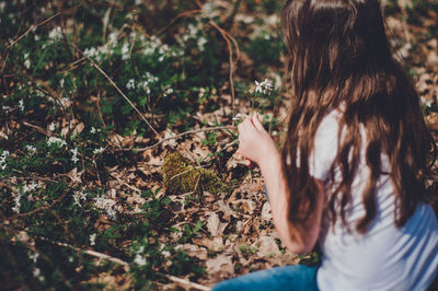 High angle view of girl holding flowers while kneeling on field