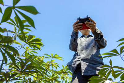 Low angle view of man photographing on plant against sky