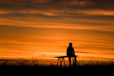 Silhouette man sitting on field against sky during sunset