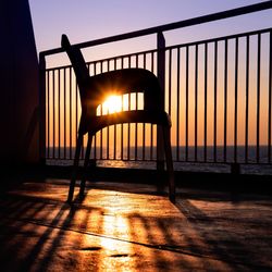 Silhouette chair against sea during sunset