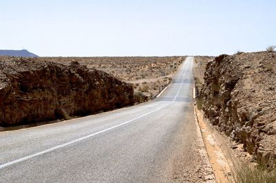 Empty road amidst land against clear sky