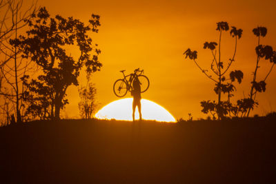 Silhouette of trees on field against orange sky