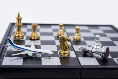 Close-up of model airplane by chess pieces on board against white background