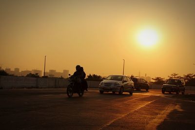 Vehicles on road against sky during sunset