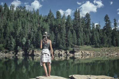 Rear view of woman standing by lake at forest