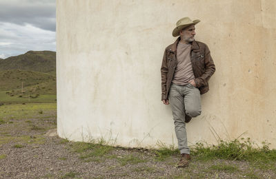 Adult man in cowboy hat standing against white wall in field