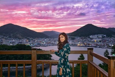 Portrait of woman standing on railing against mountains