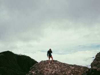 Rear view of man standing on rock against sky