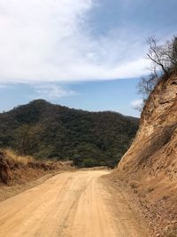 Dirt road by mountains against sky