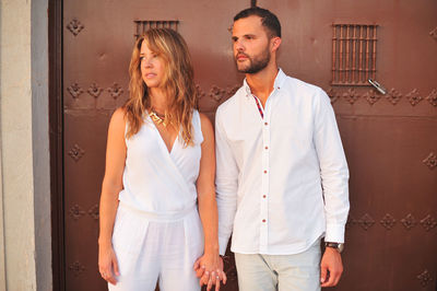 Young couple looking away while holding hands against door in city