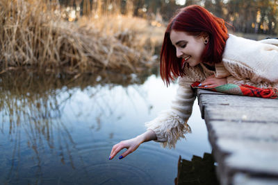 Side view of young woman sitting by lake