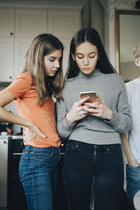 Young woman using smart phone while standing on laptop