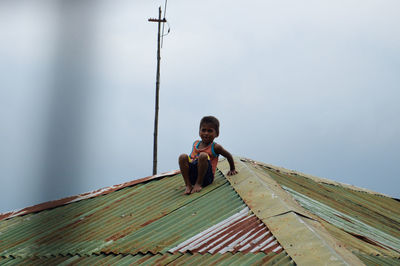 Full length portrait of happy boy on wood against sky