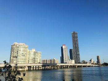 Sea by modern buildings against clear blue sky