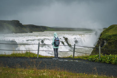 Man standing by waterfall against sky