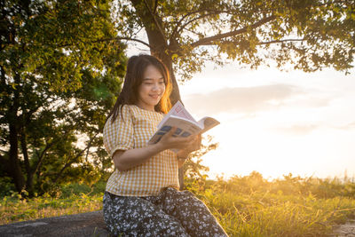 Young woman smiling while holding umbrella against trees