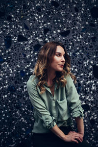 Beautiful woman looking away while standing against wall