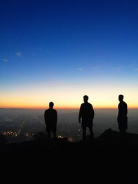 Silhouettes of three young man looking at cityscape at dusk