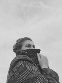 Low angle portrait of woman standing against sky during winter