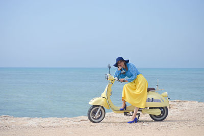Rear view of woman sitting on motorcycle on sea against clear sky
