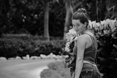 Portrait of young woman standing by plants in park