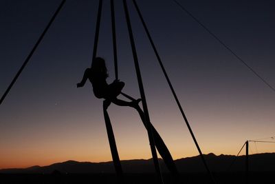 Low angle view of silhouette woman practicing acrobatics against sky during sunset