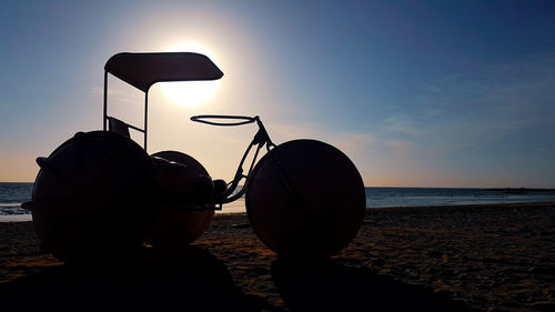 Silhouette parasols on beach against sky during sunset