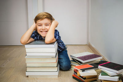 Portrait of smiling boy with books kneeling on floor at home