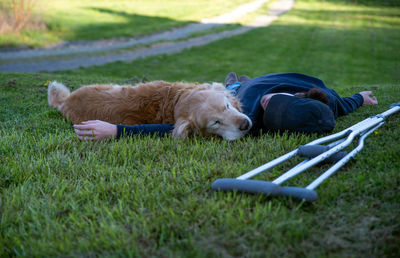 Young man and his dog lying in the grass with crutches in foreground and rural nature background 