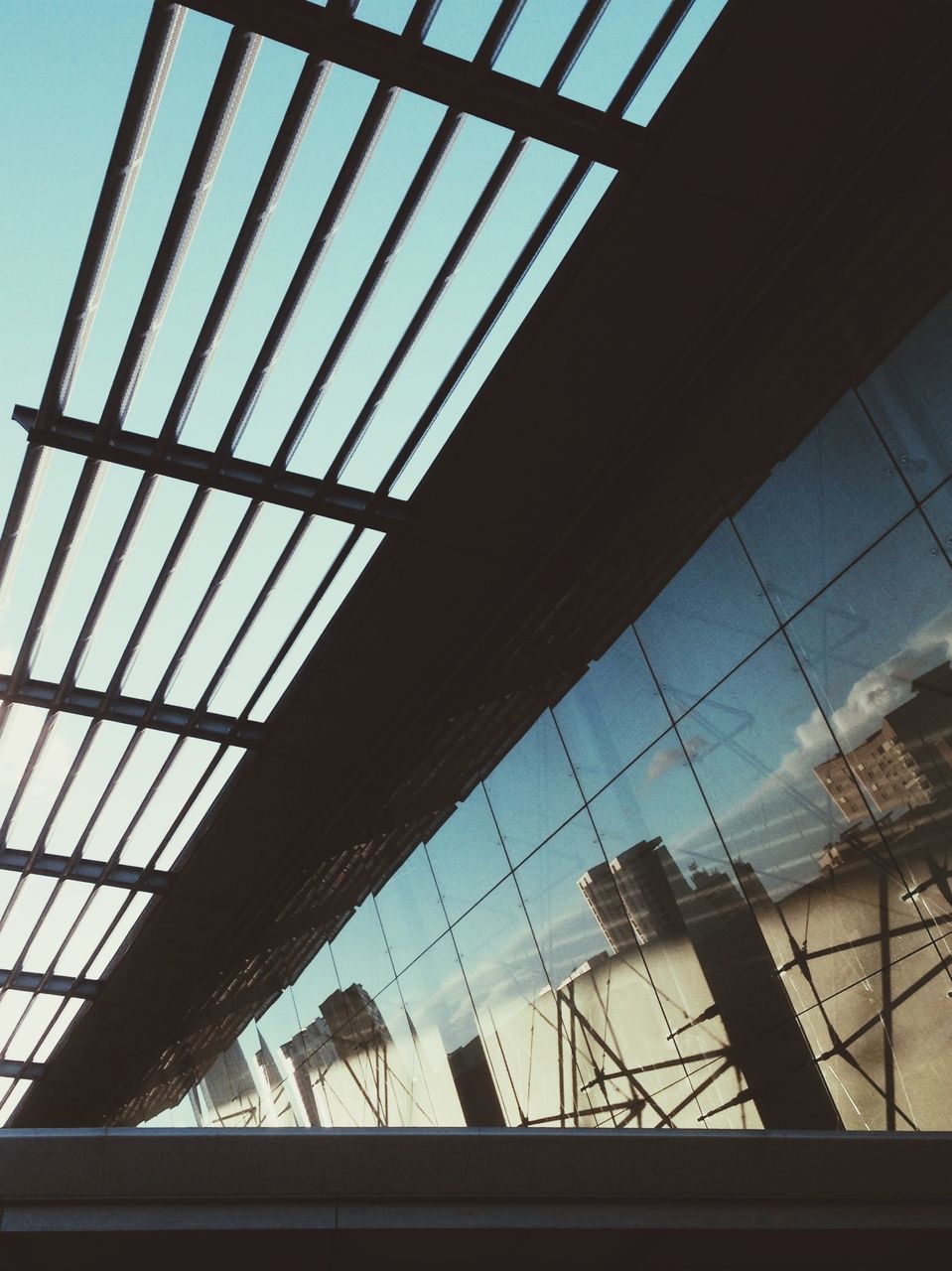 architecture, low angle view, built structure, indoors, glass - material, ceiling, window, modern, transparent, pattern, building, building exterior, glass, architectural feature, sky, skylight, reflection, day, no people, directly below