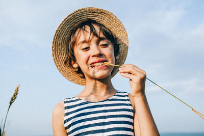 Close-up of boy holding crops in teeth against sky