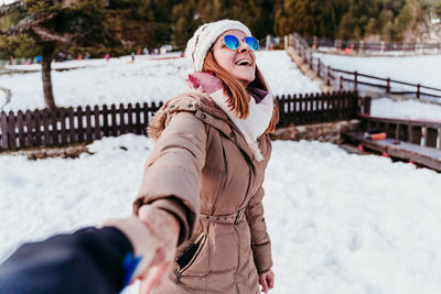 Smiling woman wearing hat and sunglasses standing in snow covered land during winter